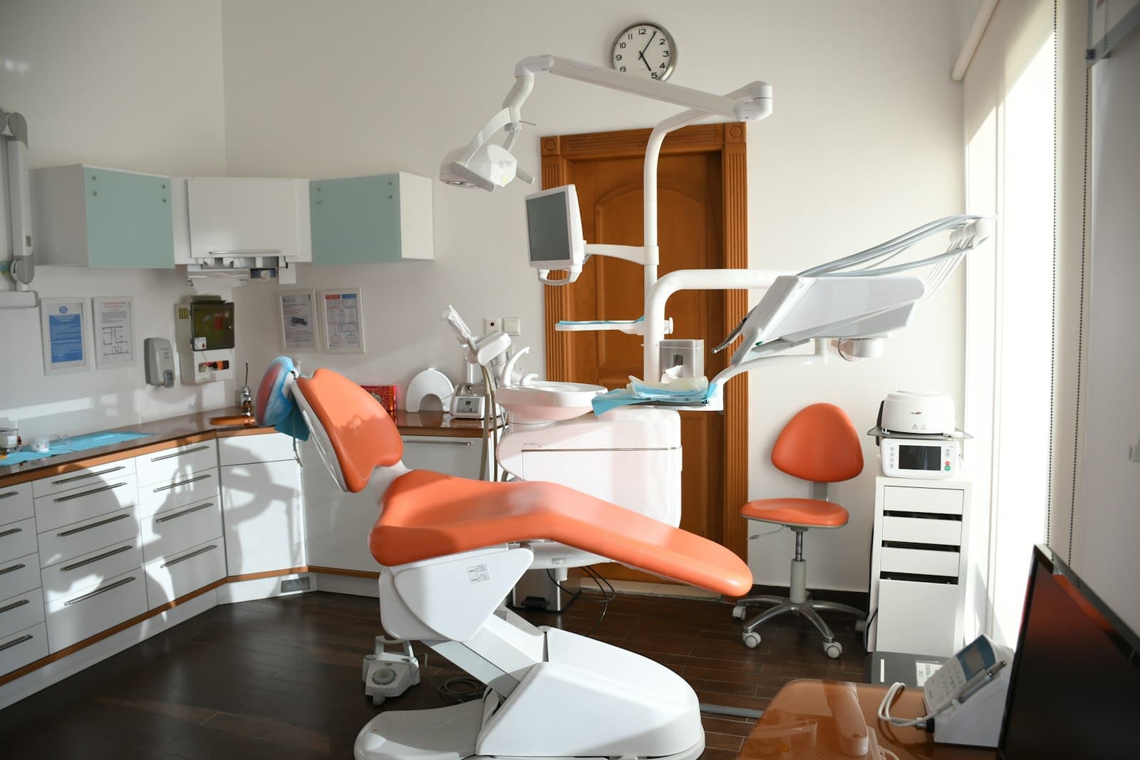 A bright, modern dental treatment room with an orange chair