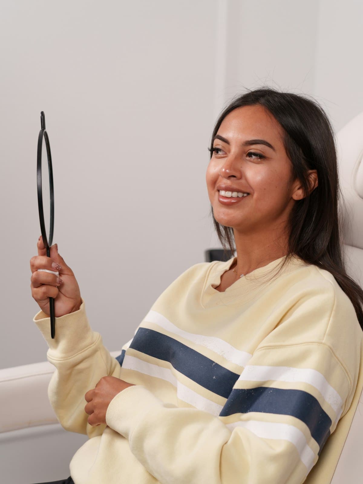 A young woman smiling at her reflection in a hand mirror